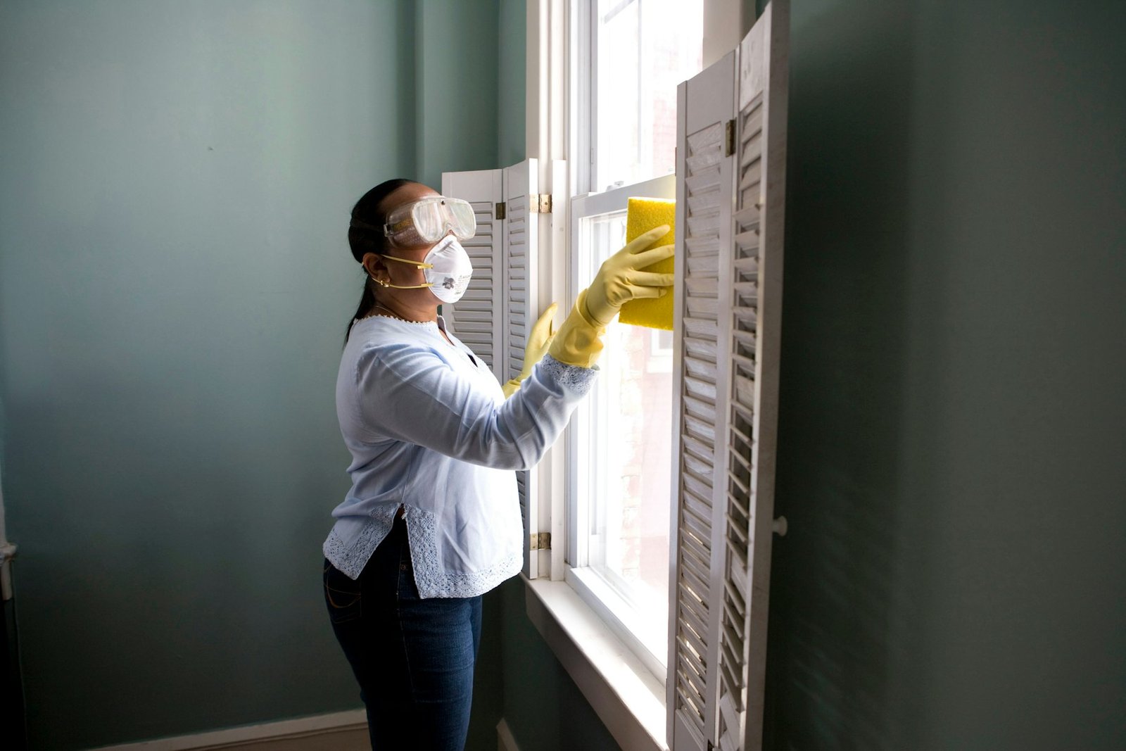 Housekeeping staff in mask and gloves cleaning window shutters