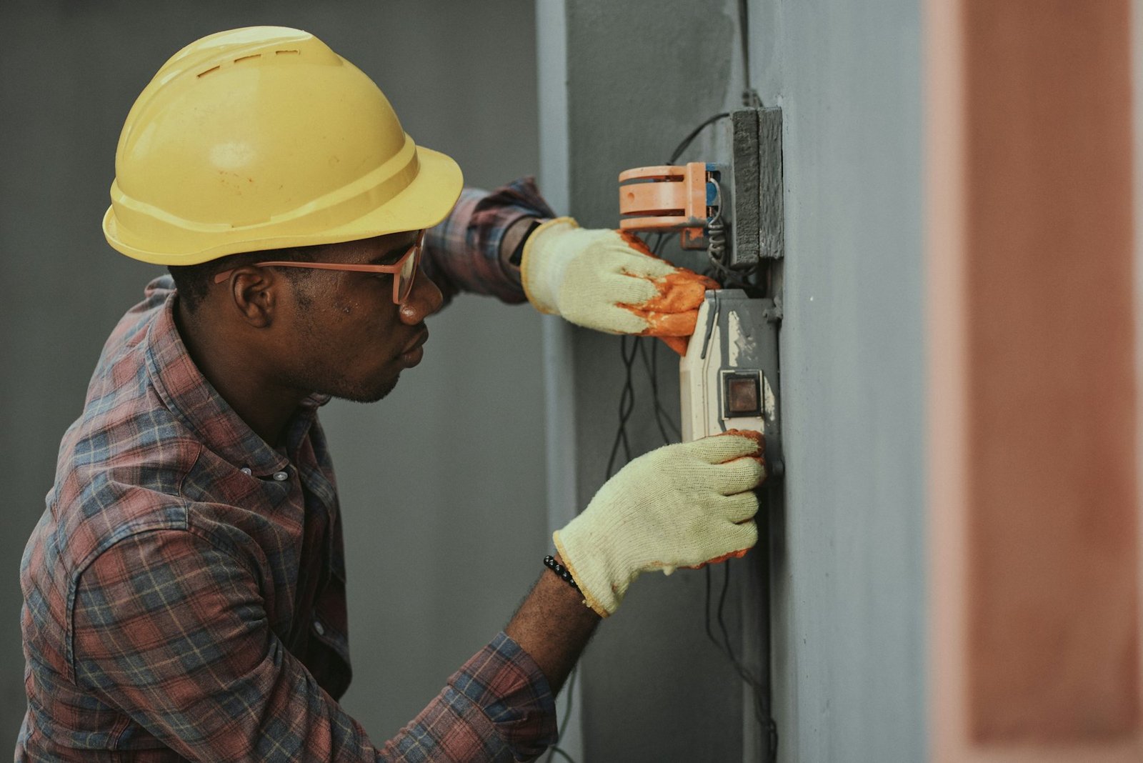 Worker in a hard hat and gloves wiring an electrical distribution box